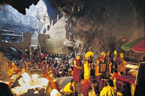 511. Inside the Maratika cave in eastern Nepal, Trulshik Rinpoche, surrounded by other lamas, offers religious robes to Dilgo Khyentse Rinpoche’s Yangsi (‘he who has come back into existence’), and gives him a name sent by the Dalai Lama: Orgyen Tendzin Jigme Lhundrup, which means ‘Spontaneous and Fearless Holder of Padmasambhava’s Teachings.’ Butter-lamps on ledges and in crevices in the rock light up the cavern, located in a remote area of the hills, a three days walk from the nearest road. Buddhists believe that Guru Padmasambhava, accompanied by his consort, the Indian princess Mandarava, was blessed here by the Buddha of Boundless Life, Amitayus, and attained a state of enlightenment beyond birth and death. The site is also venerated by Hindu ascetics, who spend nights meditating inside the cavern, their songs blending with the shrill cries of the thousands of bats that live on the high, rocky ceiling. 1995 A l’intérieur de la grotte de Maratika, à l’est du Népal, Trulshik Rinpotché, entouré d’autres lamas, offre les vêtements religieux au yangsi (celui qui est revenu dans le monde) de Dilgo Khyentsé Rinpotché et lui donne un nom choisi par le Dalaï-lama : Orguièn Tendzin Jigmé Lhündroup (Détenteur Spontané et Impavide des Enseignements de Padmasambhava). Des lampes allumées sur les corniches et dans les fissures du rocher illuminent la caverne. Maratika se trouve dans une région très isolée des collines népalaises, à trois jours de marche de la route la plus proche. Les bouddhistes pensent que le maître Padmasambhava, en compagnie de son épouse, la princesse indienne Mandarava, fut béni ici-même par Amitayus, le bouddha de la vie éternelle, et atteignit l’Eveil au-delà de la naissance et de la mort. Le site est aussi vénéré par les ascètes hindous, qui passent des nuits à méditer dans la grotte, mêlant leurs chants aux cris perçants des milliers de chauves-souris qui ont élu domicile dans les hauteurs du plafond rocheux. 1995